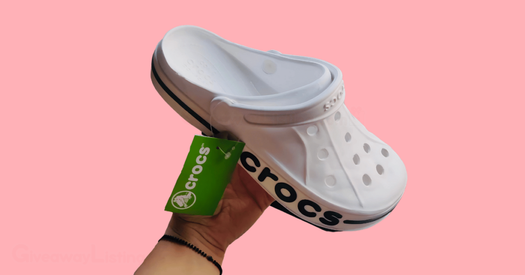 a hand holding a Crocs shoe on a light pink background.