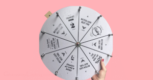 a person's hand holding a raffle wheel in a light pink background.
