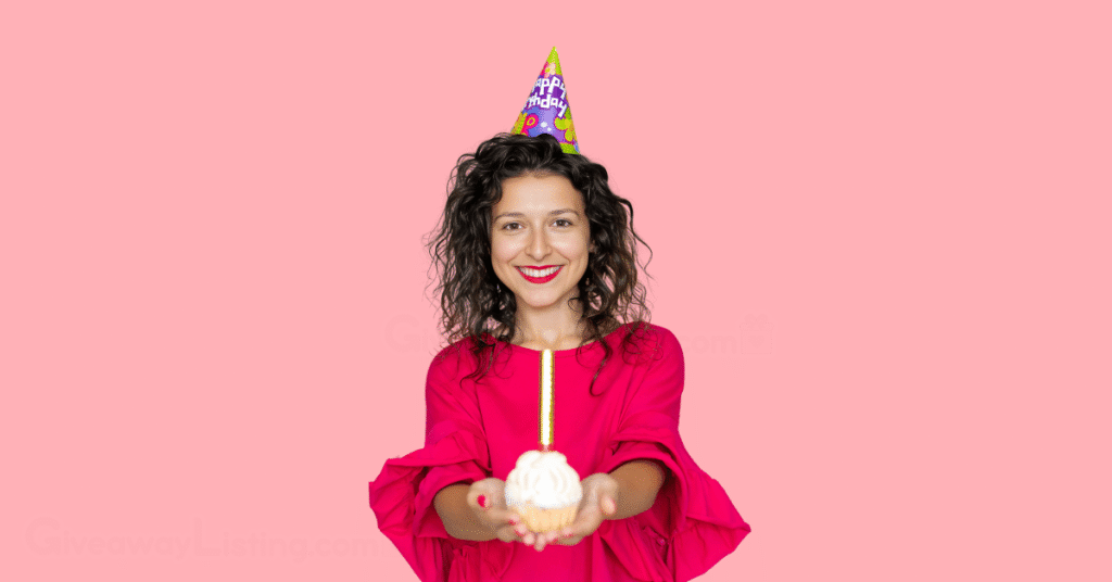 a birthday celebrant wearing a cone birthday hat and holding a cup cake.